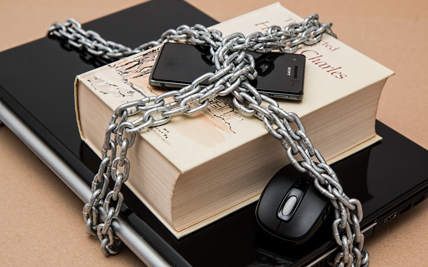 A laptop, book, smartphone, and a mice is chained on a table